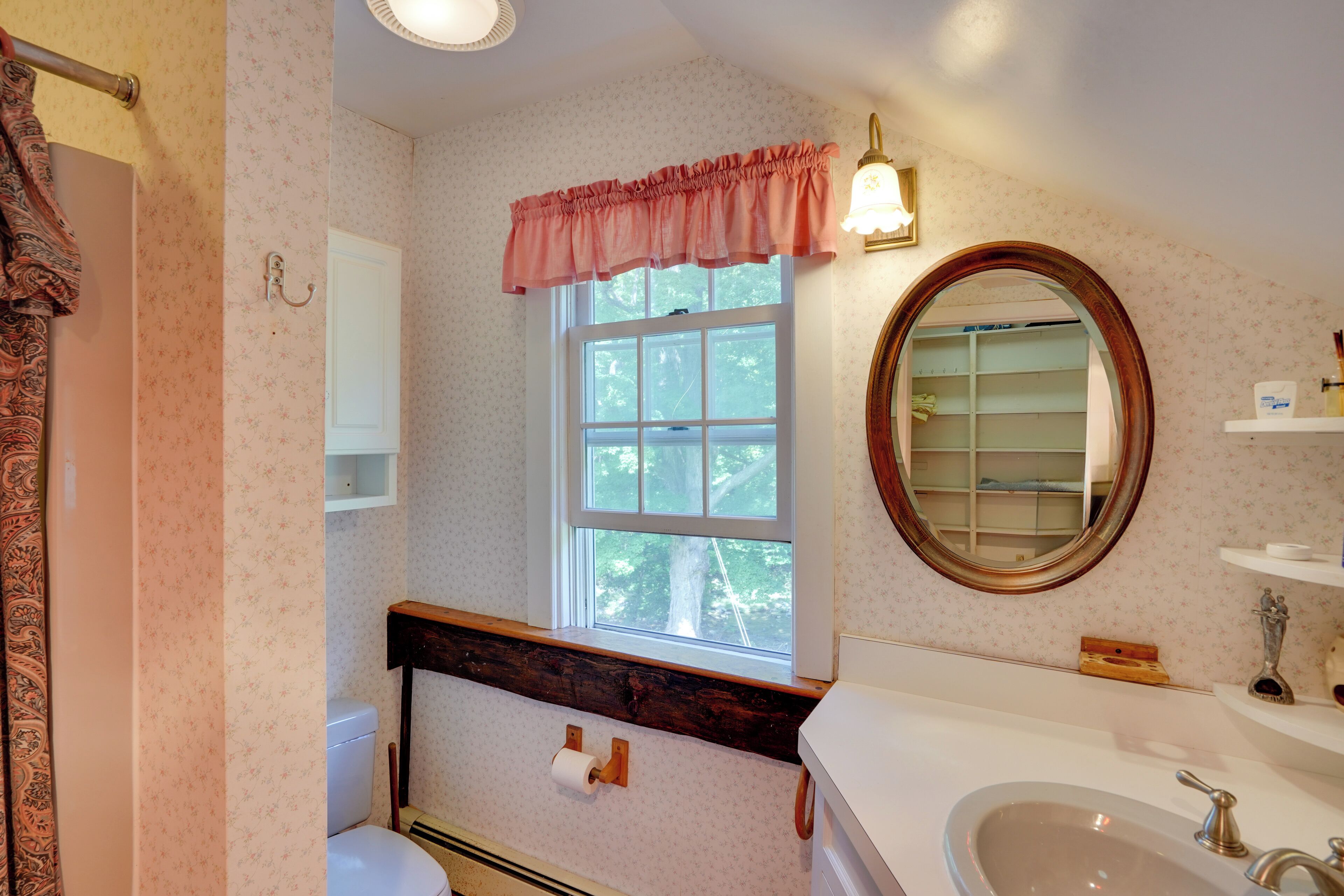 A bathroom with a toilet, sink, vanity, and a window with a view of trees.