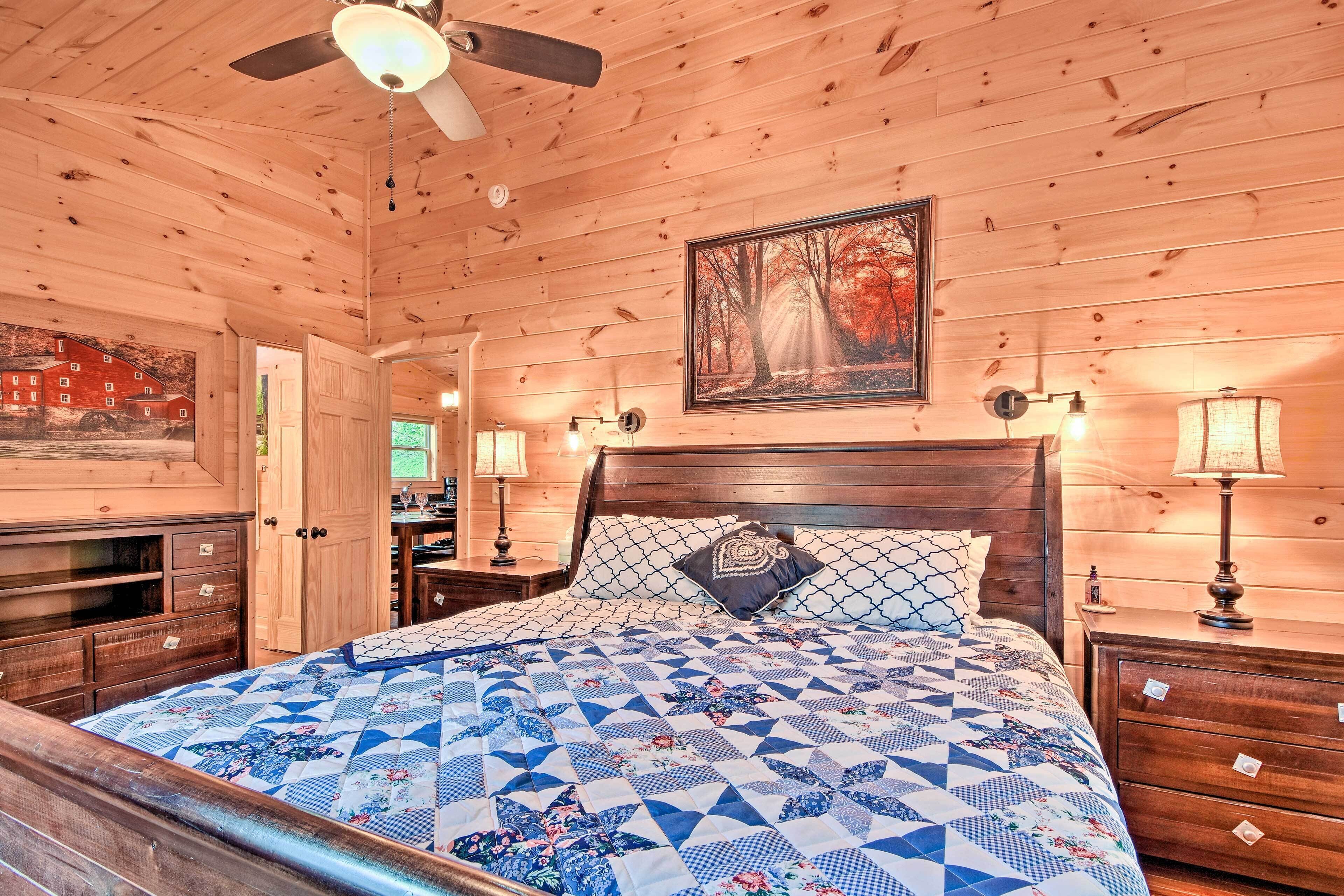 Een houten slaapkamer met een bed, nachtkastjes, een dressoir, een plafondventilator en een schilderij aan de muur.