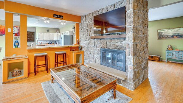 A modern kitchen with a stone fireplace, wooden bar stools, and a large TV mounted above it. - Breweries, Hiking Trails & Museums: Monument House (Monument)