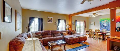 A spacious living room with a large sectional sofa, a coffee table, and a dining area with chairs and a table.