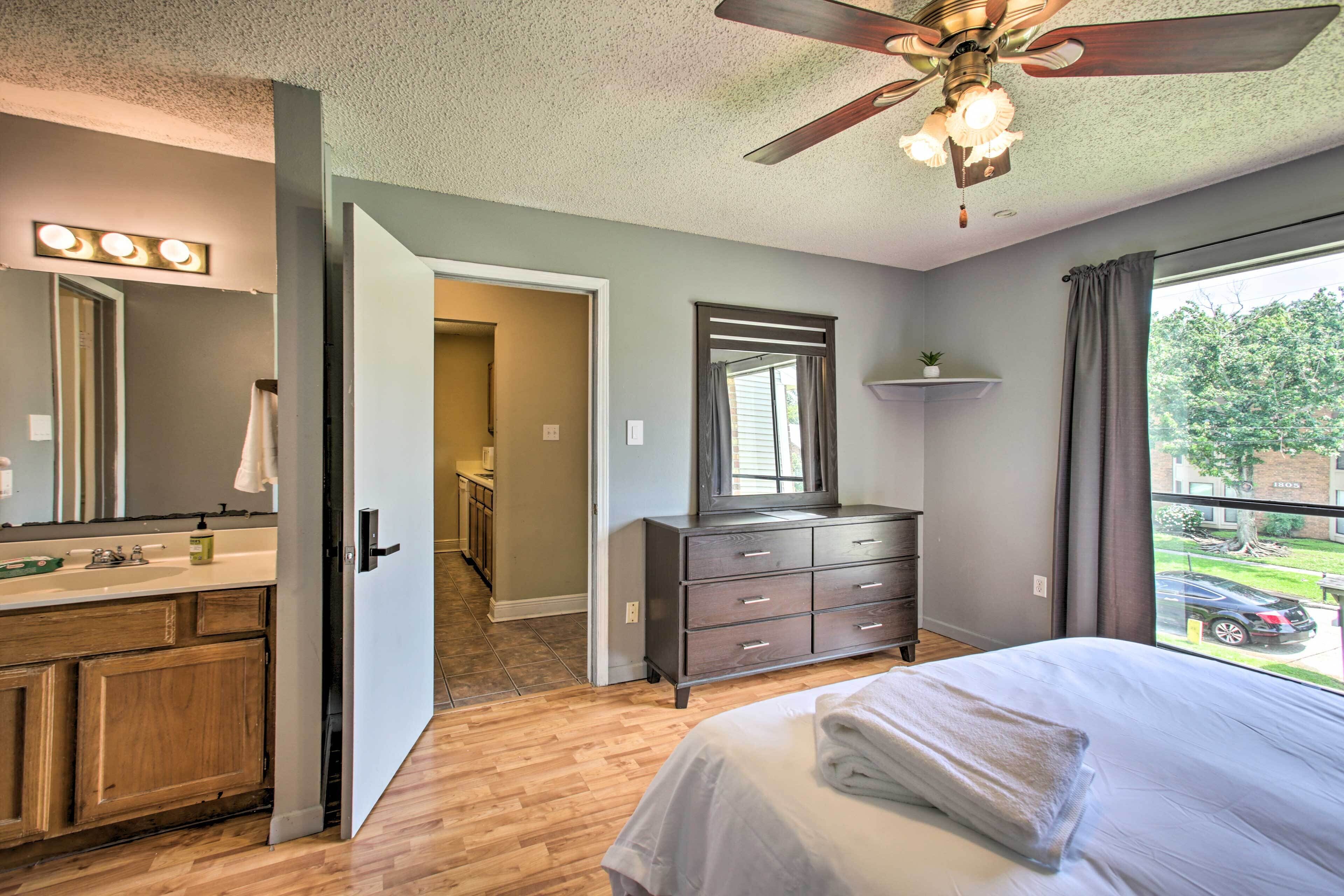 Une chambre à coucher comprenant un lit, une commode, une coiffeuse avec un miroir et un ventilateur de plafond.