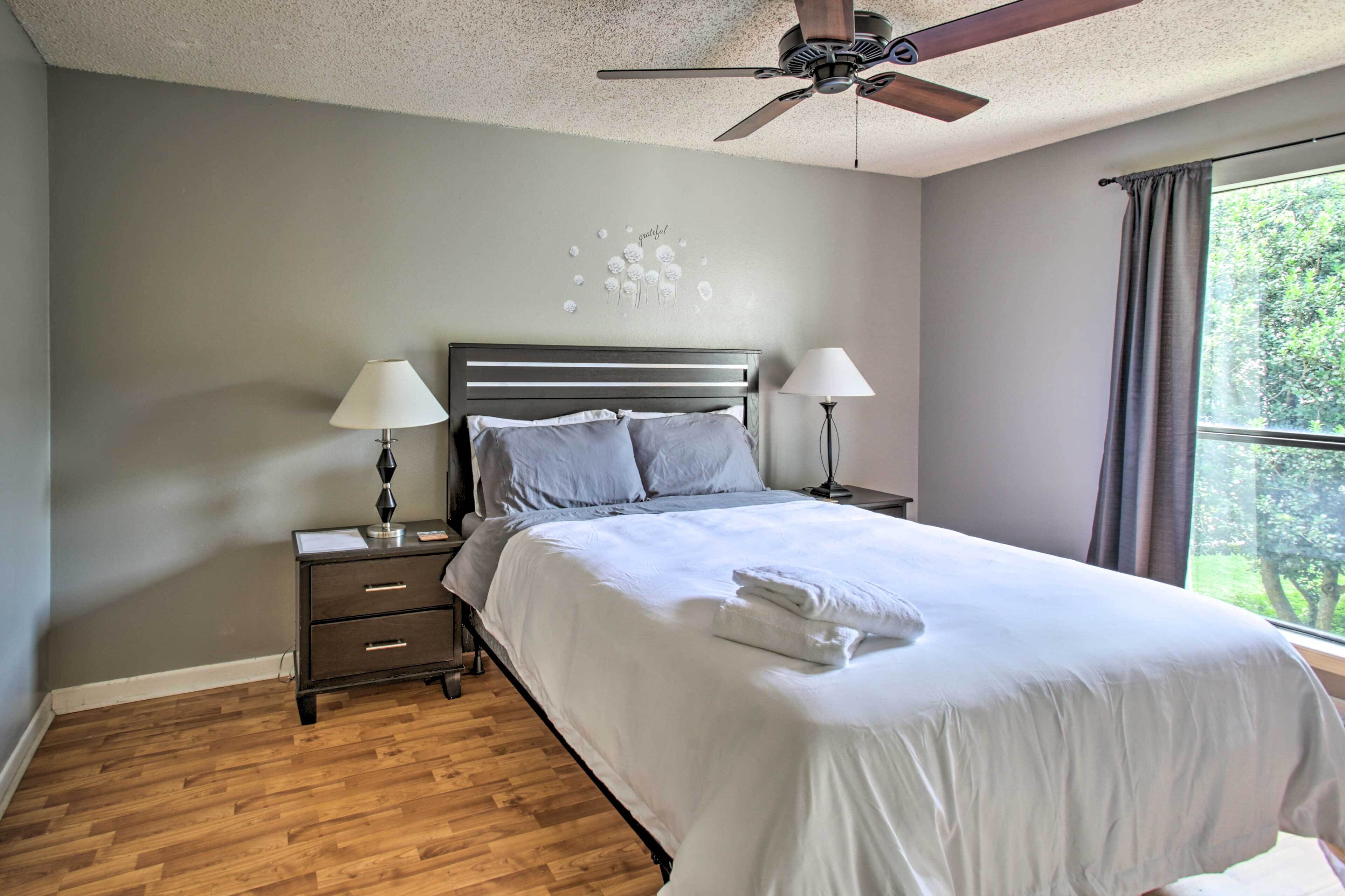 A neatly made bed with white linens, two bedside lamps, a wooden nightstand, and a ceiling fan.