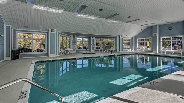 Una piscina interna con ampie vetrate, pavimento piastrellato e soffitto ventilato.