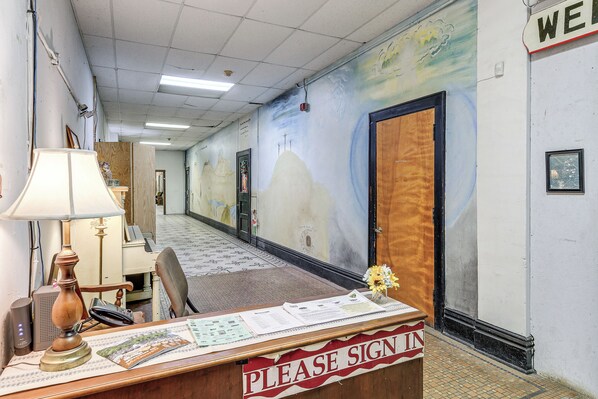 Un mostrador de recepción con un cartel que dice 'Please Sign In', una lámpara, una silla y una pared con un mural.