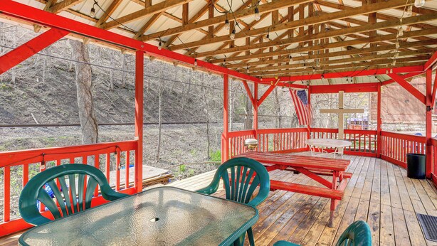 A covered outdoor deck with a table and chairs, wooden railings, and a view of a wooded area. - Family ATV Adventure Hub! Renovated Rental in Gary (Gary)