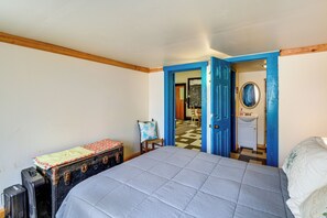 Une chambre à coucher avec un lit, une valise, une chaise et une salle de bain visible à travers une porte ouverte.