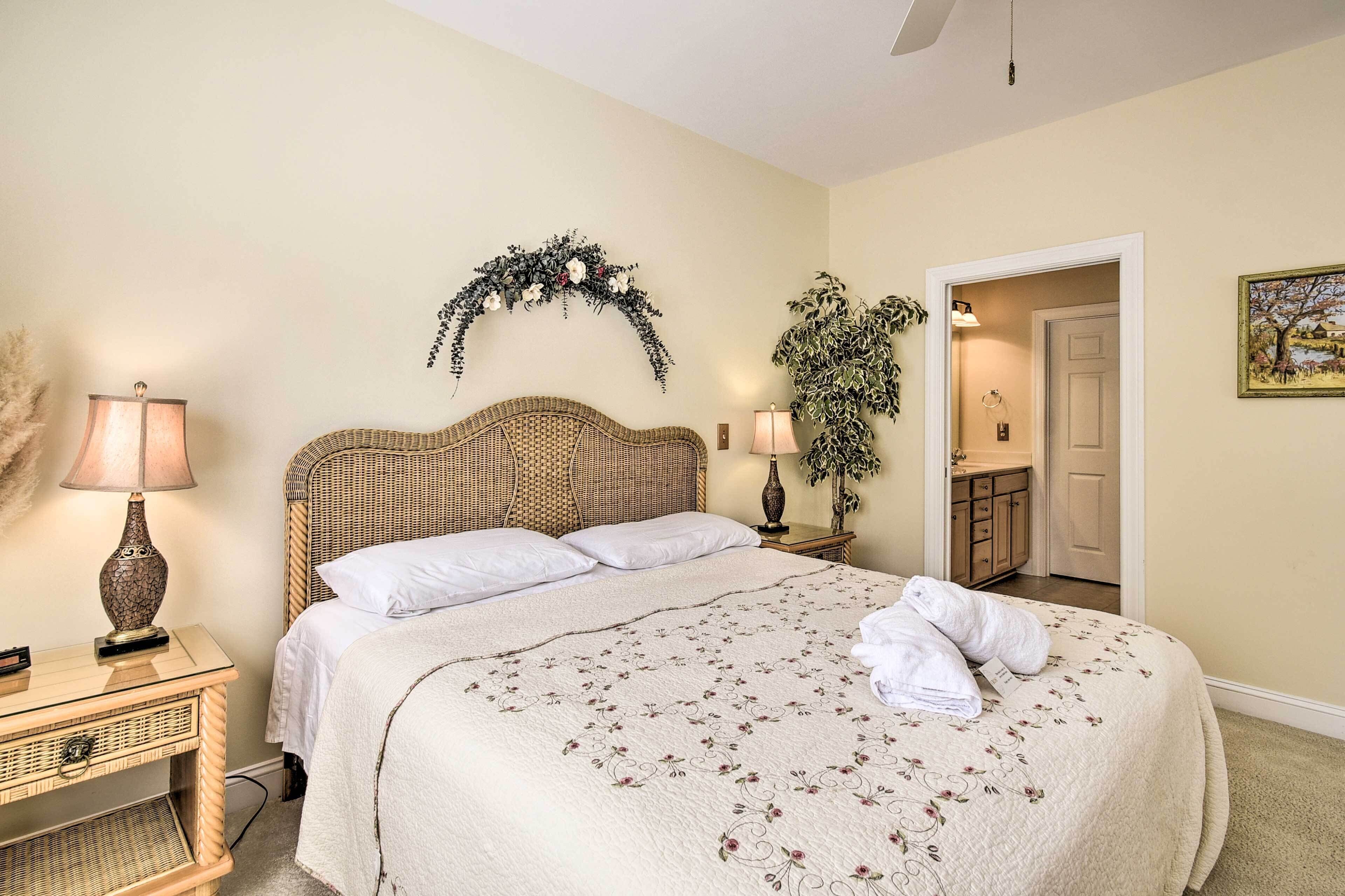 A neatly made bed with a floral bedspread, two bedside lamps, a wicker headboard, and a decorative wall arch.