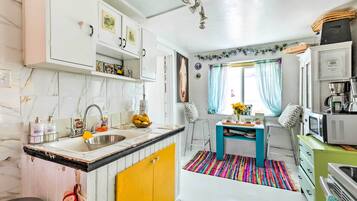 A compact kitchen with a sink, stove, and microwave. There is a small dining area with a table and chairs. The kitchen has white cabinets and a colorful rug.