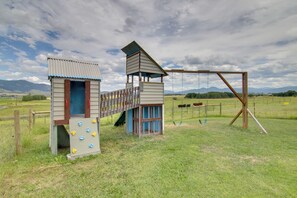 A playground with climbing structures and a slide, set in a grassy field with mountains in the background.