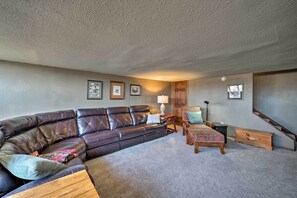 A living room with a leather sofa, a wooden coffee table, a patterned ottoman, a lamp, and a staircase.