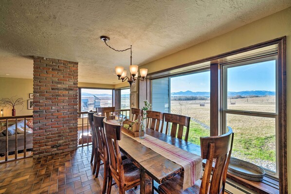 A dining area with a brick column, wooden table, and chairs, large windows with a view of the countryside.