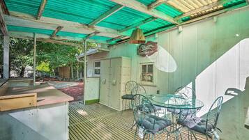 A covered outdoor area with a glass table and chairs, a wooden bench, and a hanging light fixture.