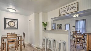 En matplats med ett träbord och stolar, en vit bardisk och en takfläkt.