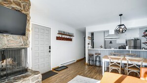 A modern kitchen with a stone fireplace, wooden flooring, and a bar area with stools. - Condo w/ Balcony & Views - Steps to Ski Shuttle! (Fraser)