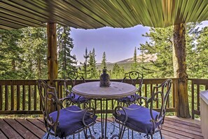 Un espace extérieur aménagé, abrité et doté d’une table ronde et de quatre chaises, entouré d’une terrasse en bois et offrant une vue sur un paysage boisé.