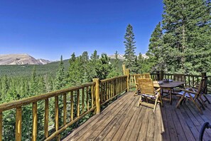 Une terrasse en bois avec une table et des chaises, offrant une vue sur une chaîne de montagnes boisée.