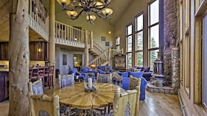 Un intérieur spacieux avec une table à manger en bois, des canapés bleus recouverts de tissu, un escalier et une cheminée en pierre.