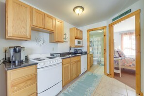 A compact kitchen with wooden cabinets, a stove, a microwave, and a sink. - Wells Vacation Rental ~ 1 Mi to Beach Access! (Wells)