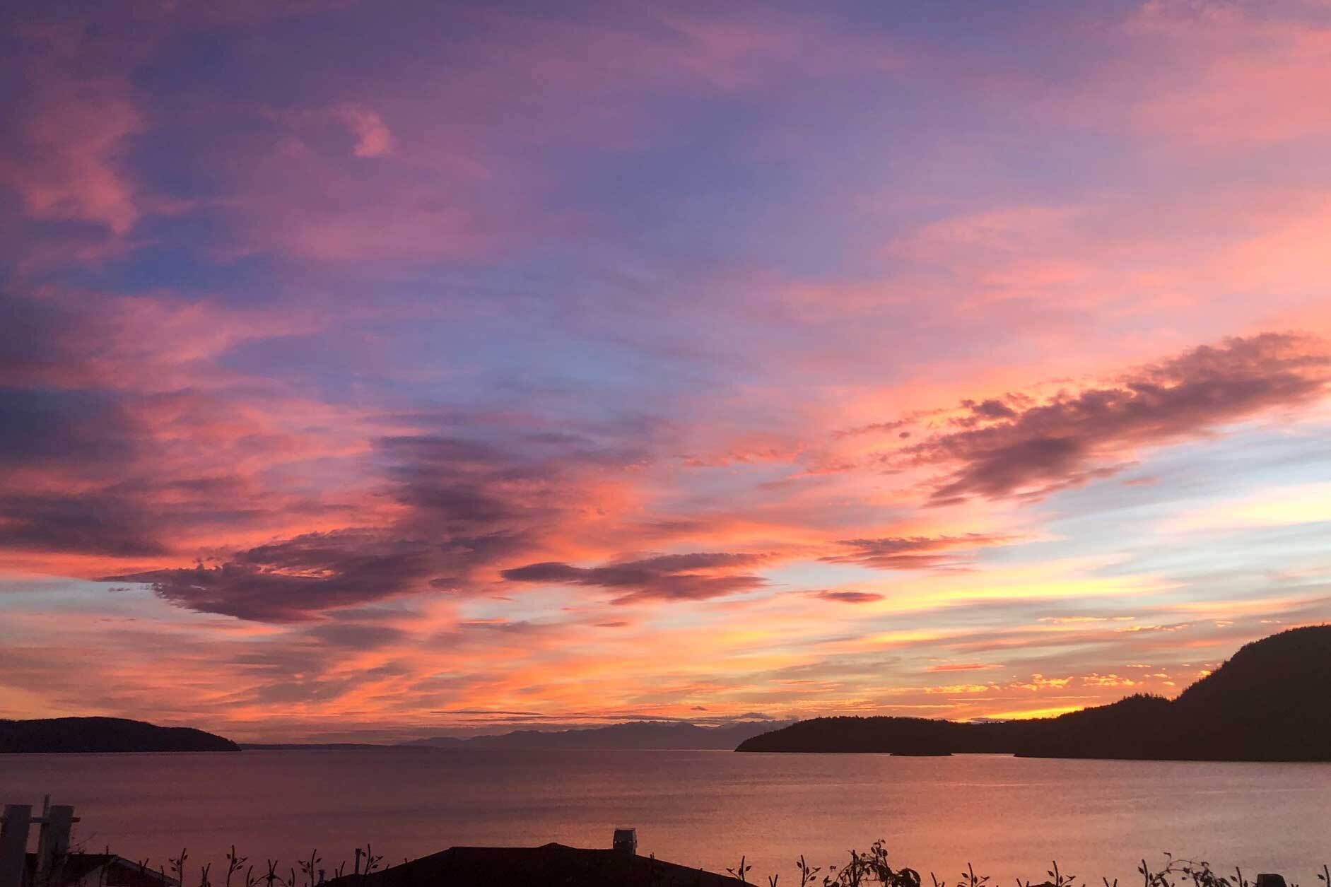 A sunset over a calm body of water with distant landforms.