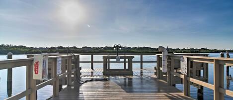 A wooden pier extending into calm water with a bench and fire extinguisher in the center.