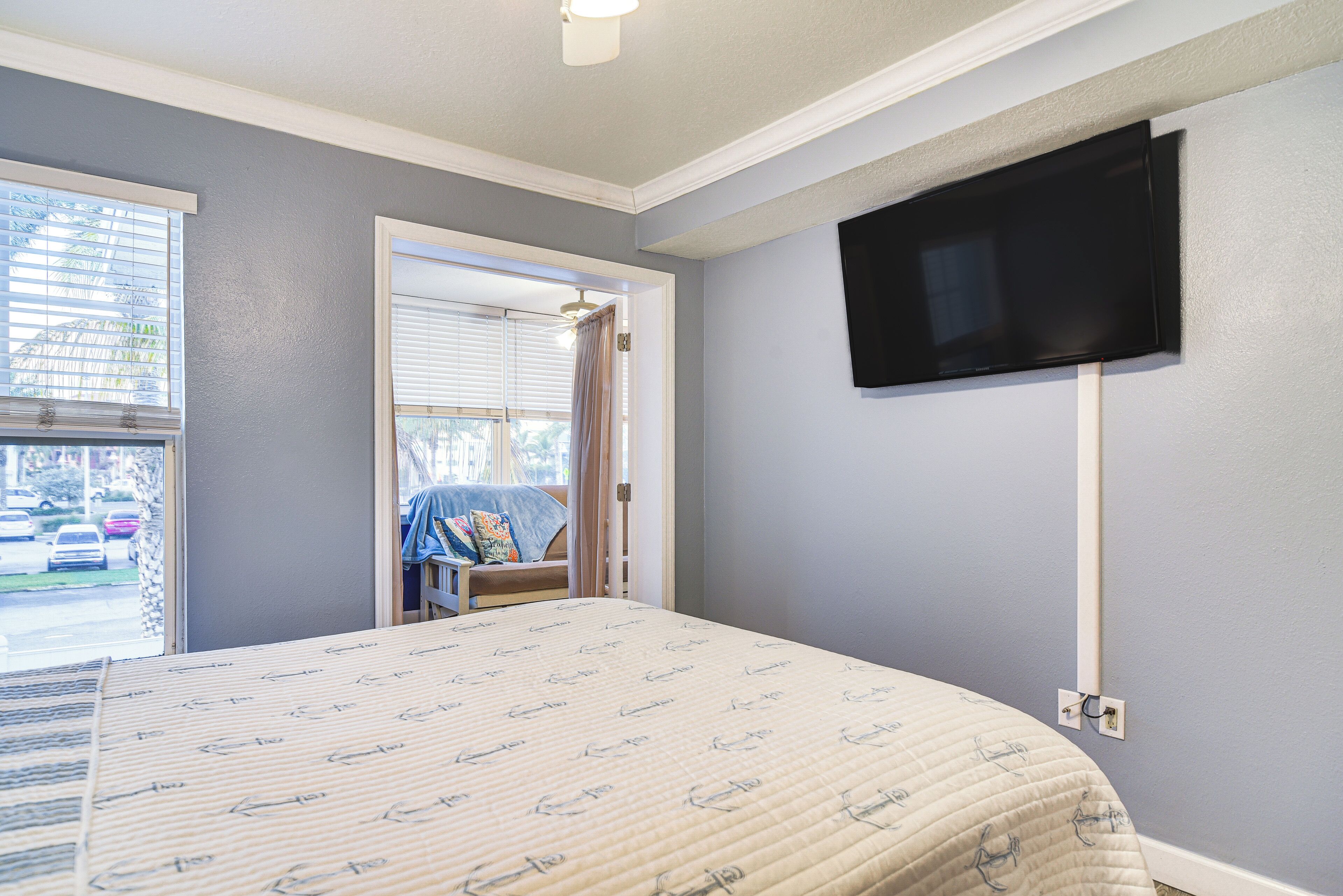 Une chambre à coucher avec un lit, un téléviseur fixé au mur et une fenêtre avec des stores.