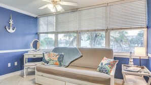 A room with a beige sofa, a white side table, a small white chair, a ceiling fan, and a window with blinds. - Resort Condo w/ Beach Access in Indian Shores! (Indian Shores)