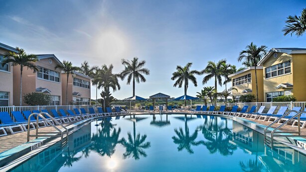 A swimming pool with blue lounge chairs, palm trees, and a clear sky. - Resort Condo w/ Beach Access in Indian Shores! (Indian Shores)