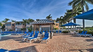A poolside area with sun loungers and umbrellas, palm trees, and a covered seating area. - Resort Condo w/ Beach Access in Indian Shores! (Indian Shores)