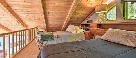 A cozy attic bedroom with a sloped ceiling, a wooden bed, a nightstand, and a window with a view of greenery.