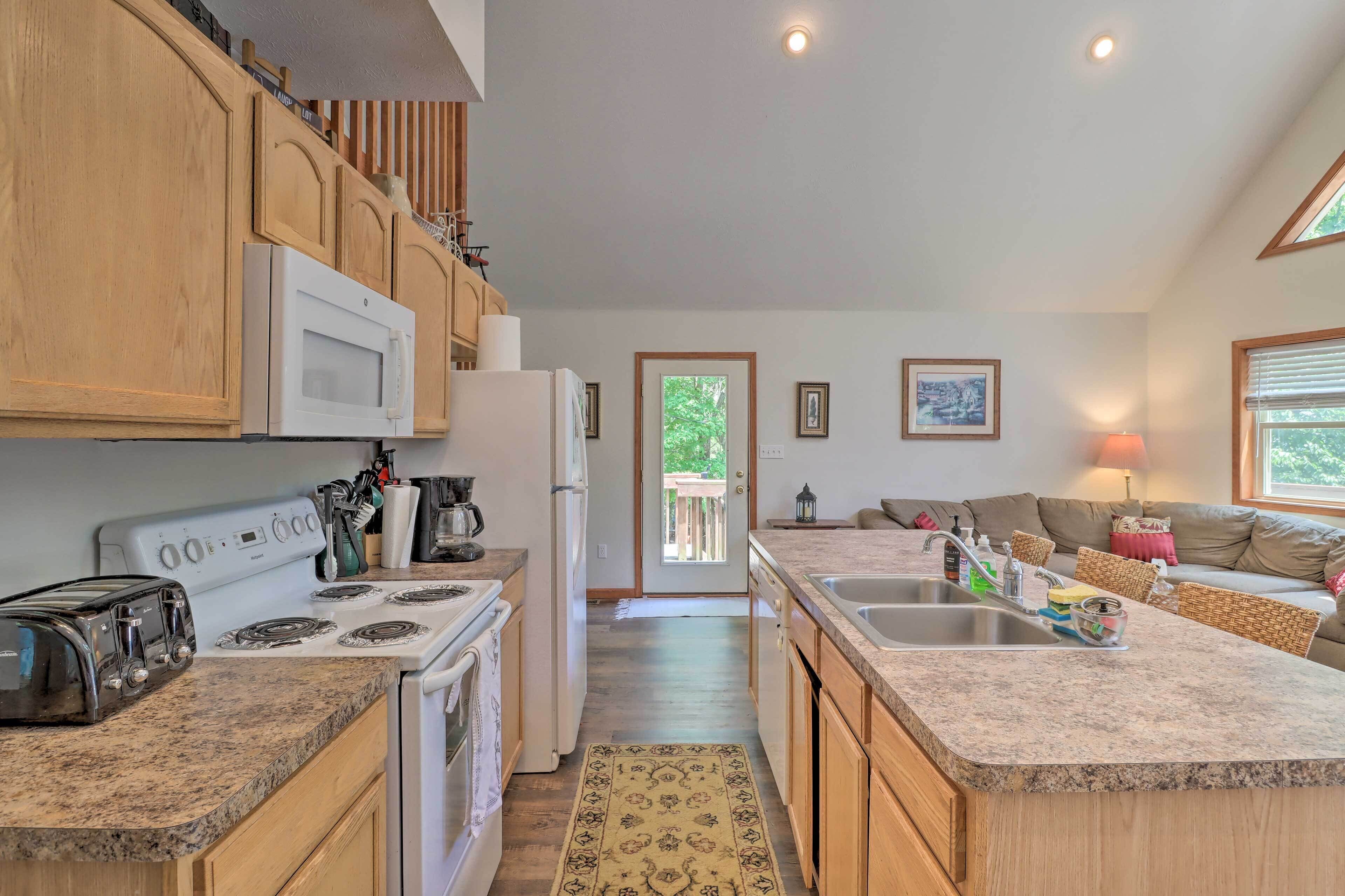 A kitchen with wooden cabinets, a microwave, a stove, a refrigerator, and a toaster. There is a rug on the floor and a window with blinds.