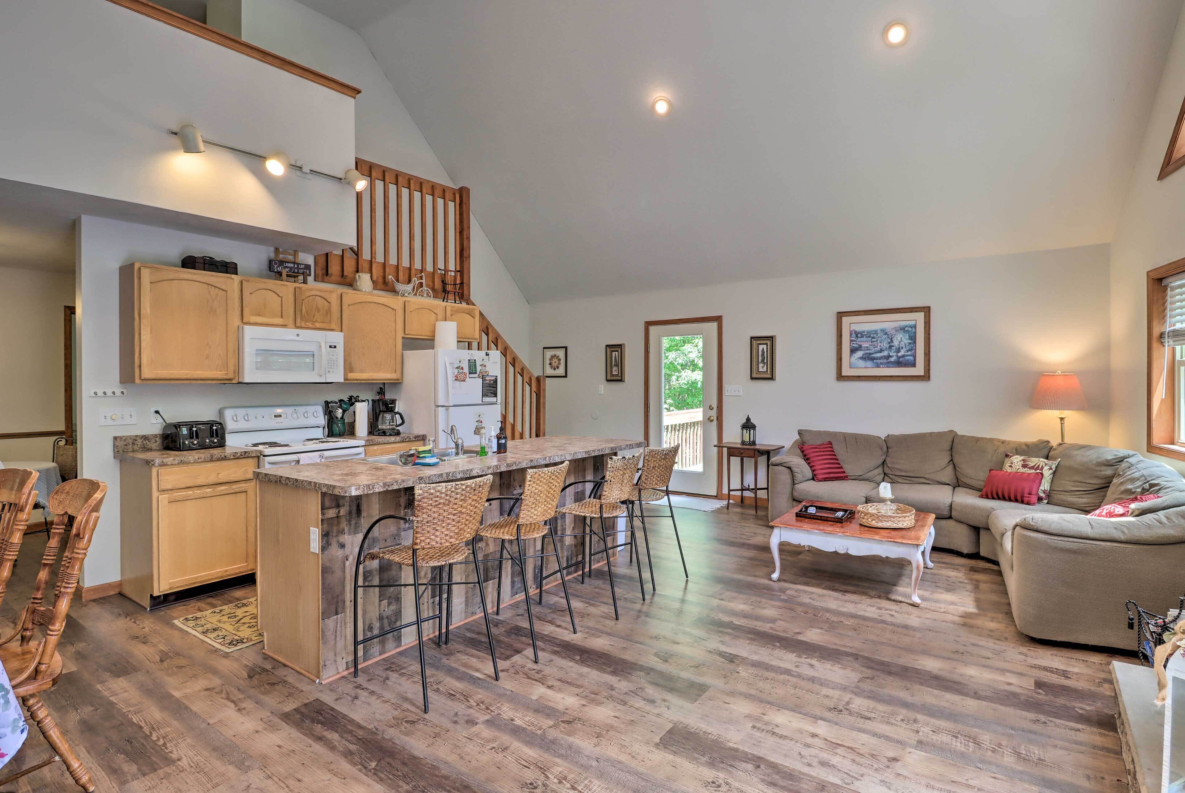 A spacious living area with a kitchen, wooden flooring, a dining table, and a sofa.