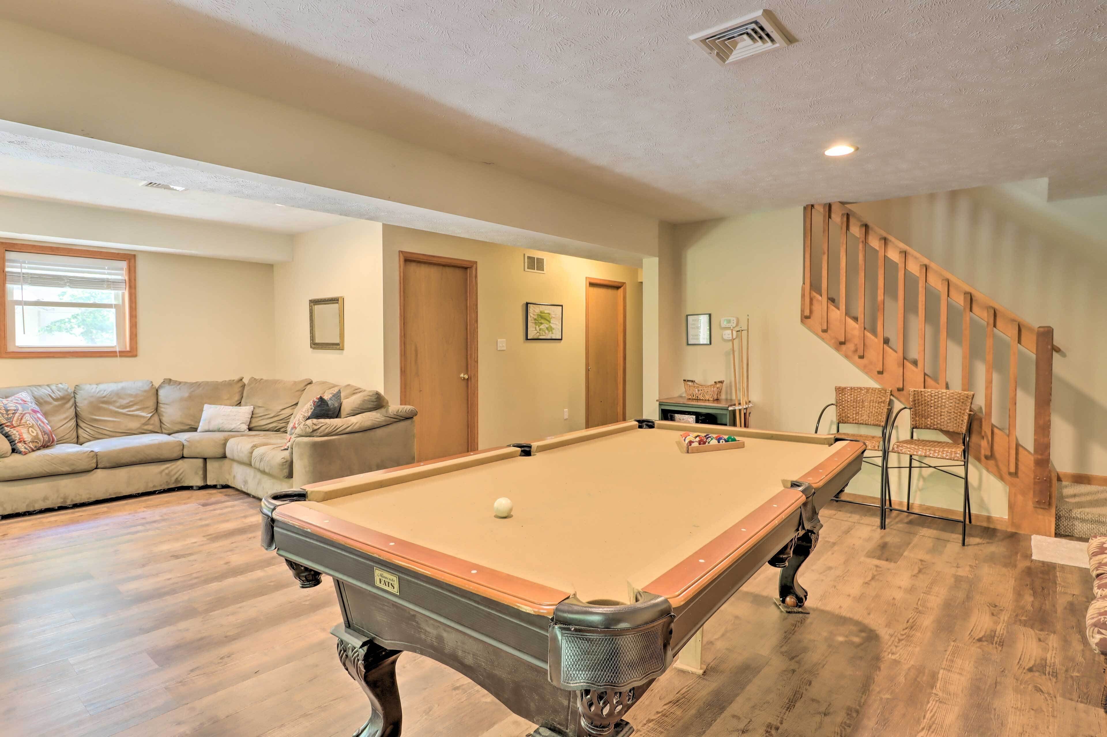 A pool table in a living room with a sofa and a staircase.