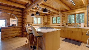 Interno di una baita con isola della cucina, sgabelli da bar, mobili in legno e illuminazione a sospensione.