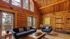 Interno di una baita di legno con due divani, un tavolino da caffè e un'ampia porta in legno.