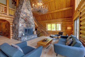 L’intérieur d’une cabane en rondins, avec une cheminée en pierre, un escalier en bois et des canapés bleus recouverts de tissu.
