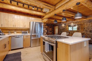 A modern kitchen with wooden cabinets, stainless steel appliances, and a stone accent wall. - Hand-crafted Cabin w/ Whitefish Lake Views! (Whitefish)