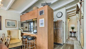 A cozy kitchen with a wooden island, bar stools, a dining area with a yellow chair, and a clock on the wall. - Waterfront White Lake Vacation Rental! (Kauneonga Lake)