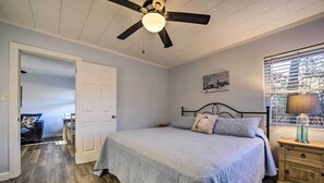 Un dormitorio con cama, ventilador de techo, mesita de noche y ventana con persianas.