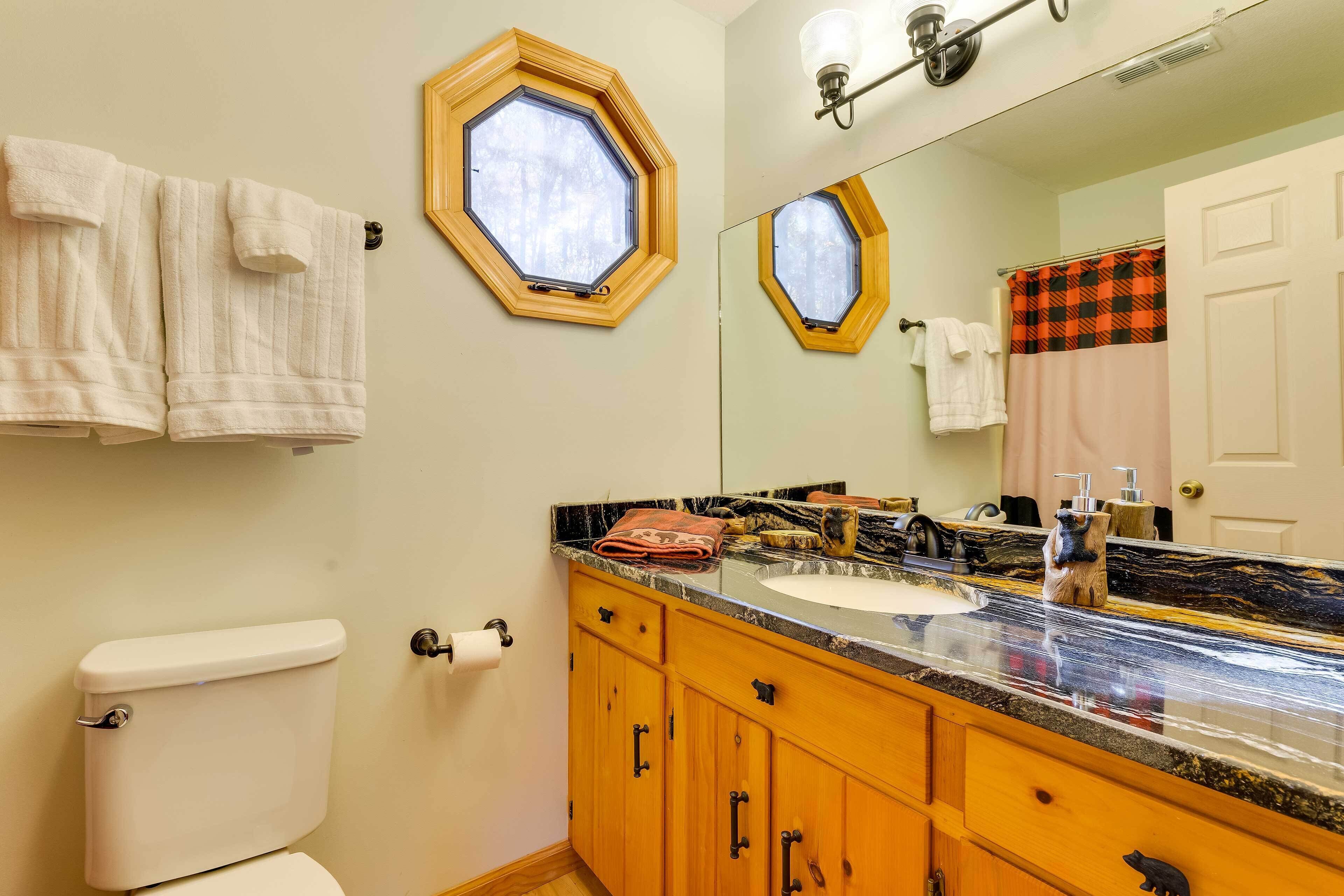 Een badkamer met toilet, wastafel met een marmeren blad, houten kastjes, een spiegel en een raam met houten omlijsting.