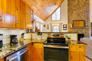 A kitchen with wooden cabinets, a stone wall, a large window, and a built-in oven. - Smoky Mountain Cabin w/ Fire Pit: Hike & Fish! (Murphy)