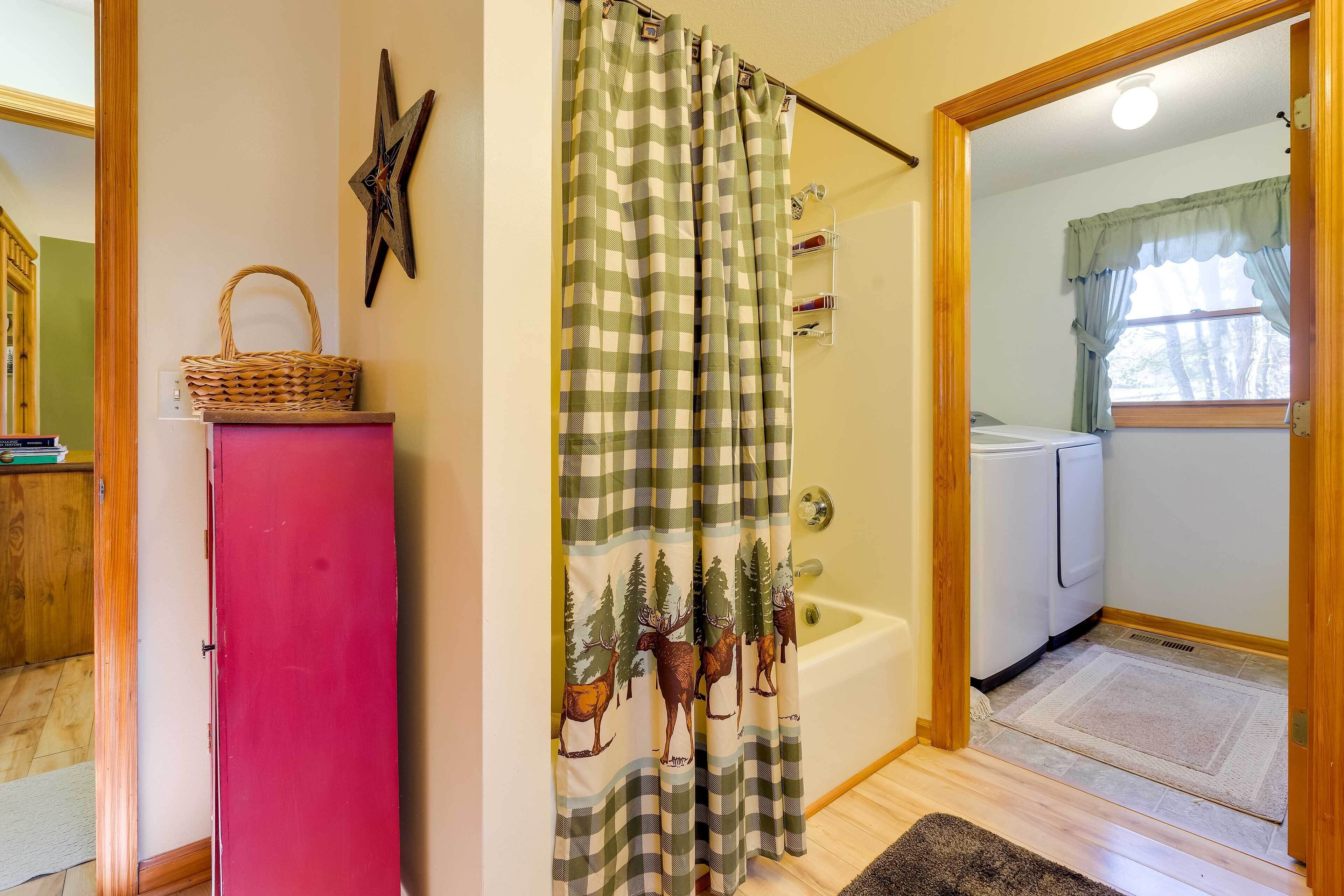Une salle de bain avec un rideau de douche à carreaux, un meuble rouge, une décoration en forme d’étoile et une fenêtre donnant sur des arbres.