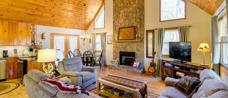 A spacious living room with a stone fireplace, wooden ceiling, and a television.