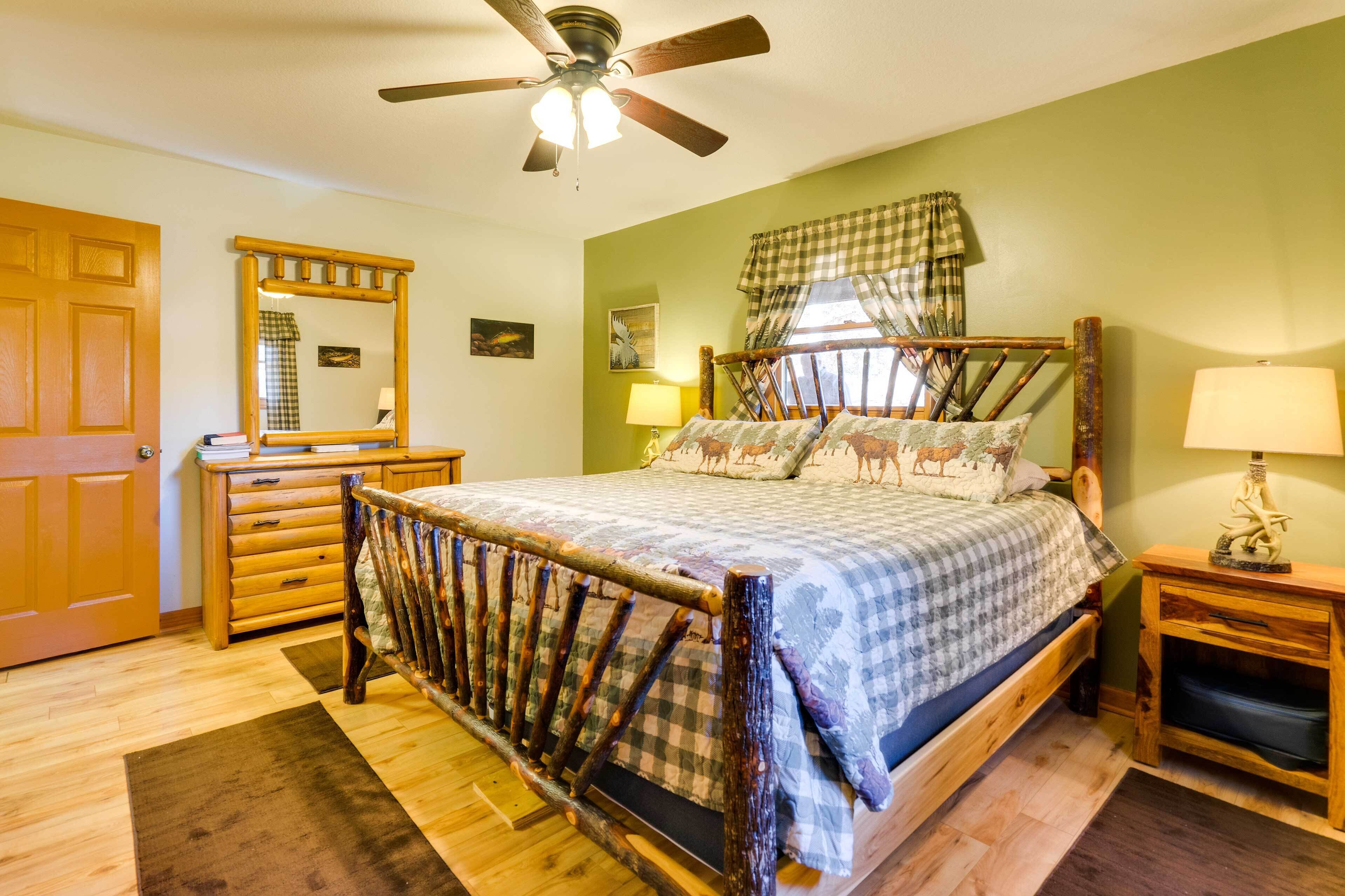 Een slaapkamer met een houten bed, een plafondventilator, een dressoir en een raam met gordijnen.