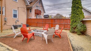 Un jardin avec un foyer extérieur, des chaises de jardin et un grand arbre à feuilles persistantes.