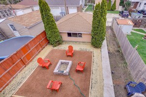 Ein Garten mit Feuerstelle, vier Adirondack-Stühlen und einem Trampolin.