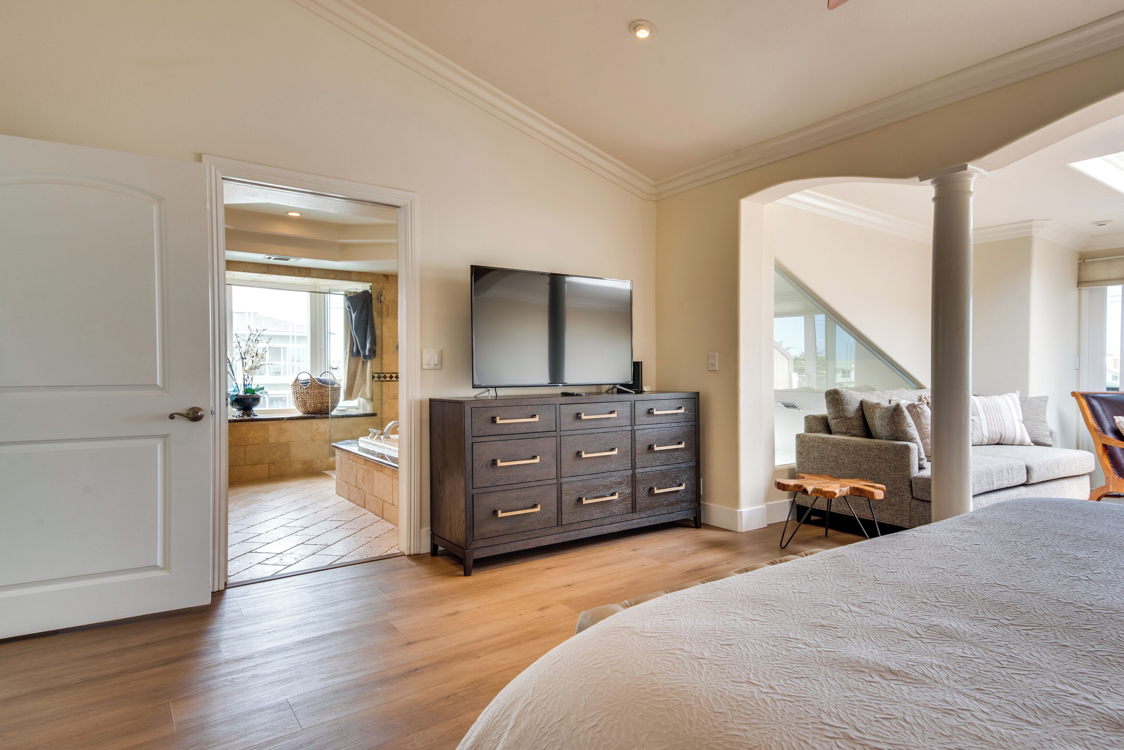 Une chambre à coucher avec un grand lit, une commode surmontée d’un téléviseur à écran plat, un escalier et une vue sur l’extérieur.