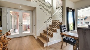 A modern interior with a wooden staircase, a dining area with a table and chairs, and a view of the outside. - Luxurious Channel Islands Harbor Home w/ Boat Dock (Oxnard)