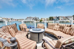 A waterfront patio with striped sofas and a round table, overlooking a marina and residential buildings. - Luxurious Channel Islands Harbor Home w/ Boat Dock (Oxnard)