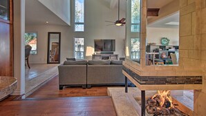 A spacious living room with a fireplace, a large window, and a television. - Luxurious Channel Islands Harbor Home w/ Boat Dock (Oxnard)