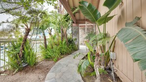 A stone pathway leading to a wooden door, surrounded by lush tropical plants and a view of the water. - Luxurious Channel Islands Harbor Home w/ Boat Dock (Oxnard)